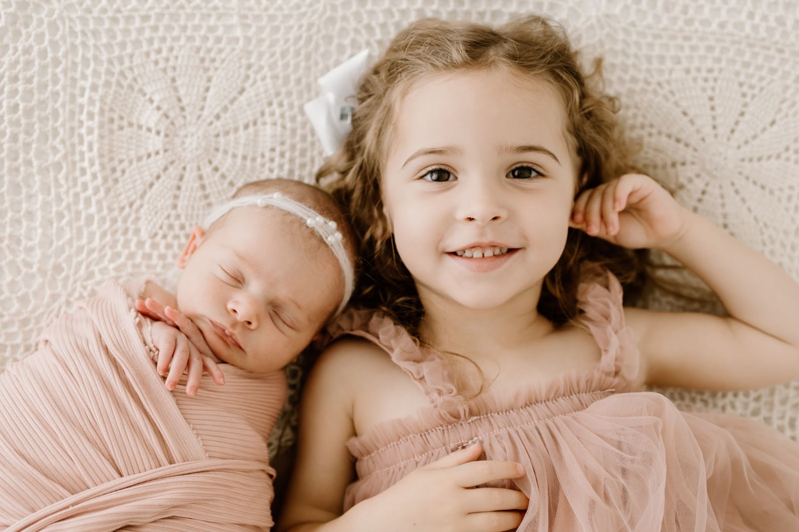 Newborn baby asleep next to older sister looking at the camera